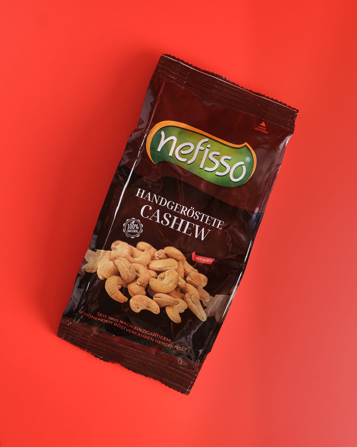Echte Aufnahme einer braunen Nefisso Cashewpackung auf korallrotem Hintergrund