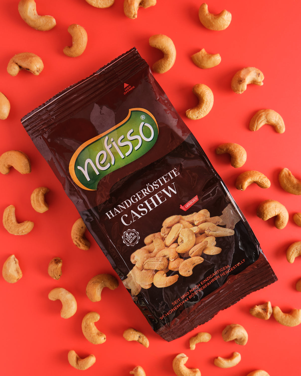 Nefisso Cashews in brauner Verpackung mit Cashewnüssen auf korallrotem Hintergrund