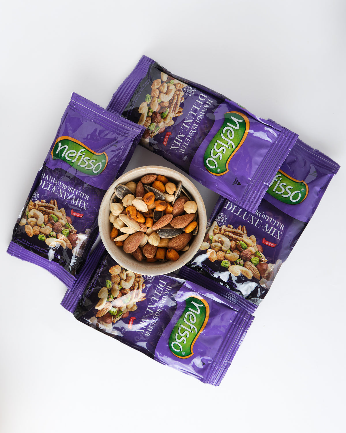 Nefisso Deluxe Mix in violetten Beuteln rund um eine Schale mit Nussmischung