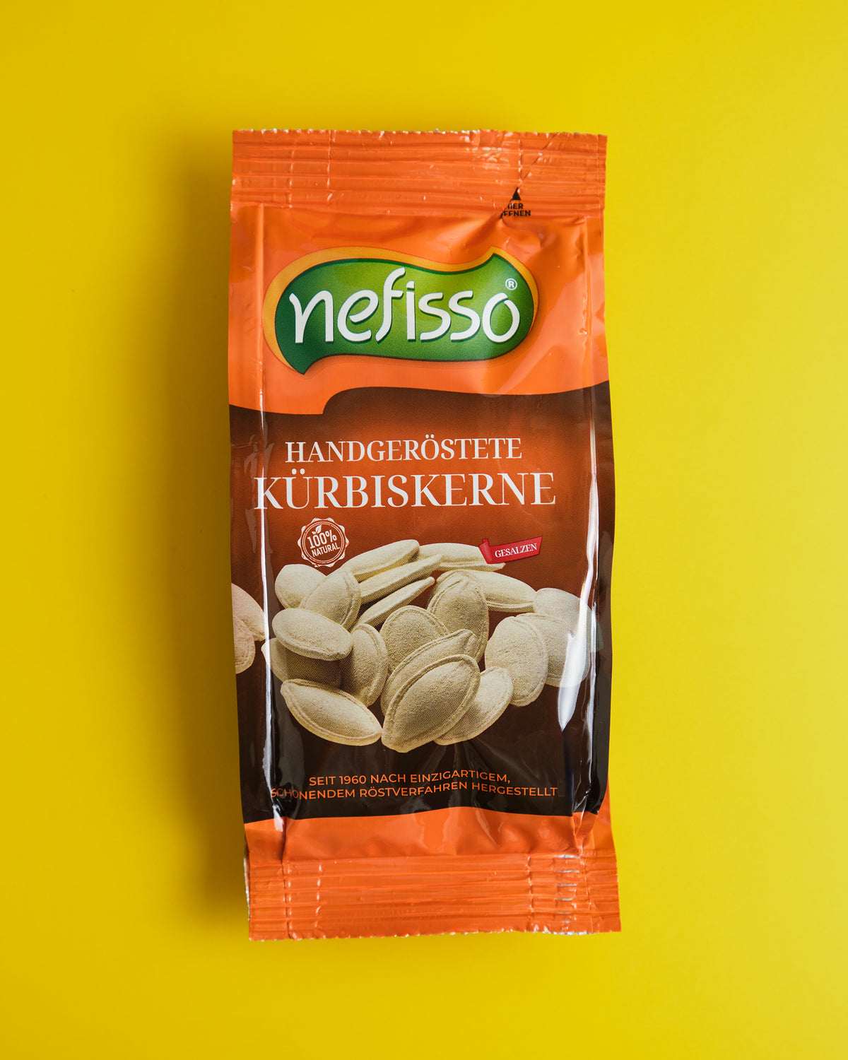 Echte Aufnahme einer orangefarbenen Nefisso Kürbiskernpackung auf gelbem Hintergrund