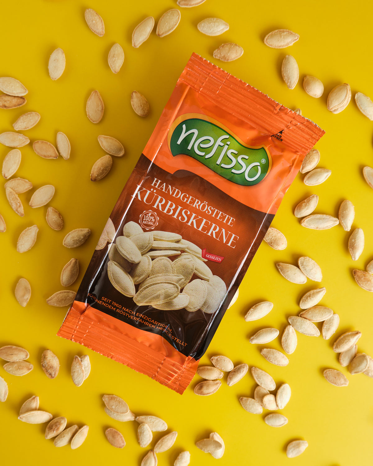 Nefisso Kürbiskerne in orangefarbener Verpackung mit Kürbiskernen auf gelbem Hintergrund