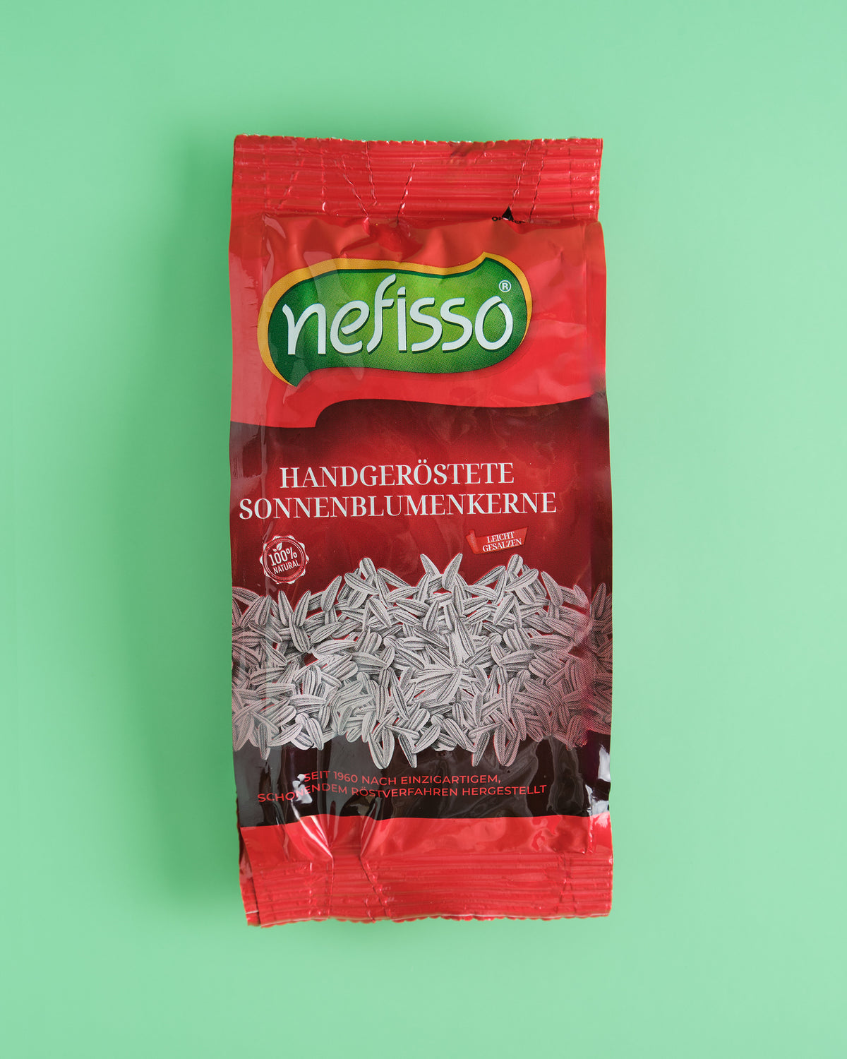 Echte Aufnahme klassischer Nefisso Sonnenblumenkerne in roter Packung auf mintgrünem Hintergrund