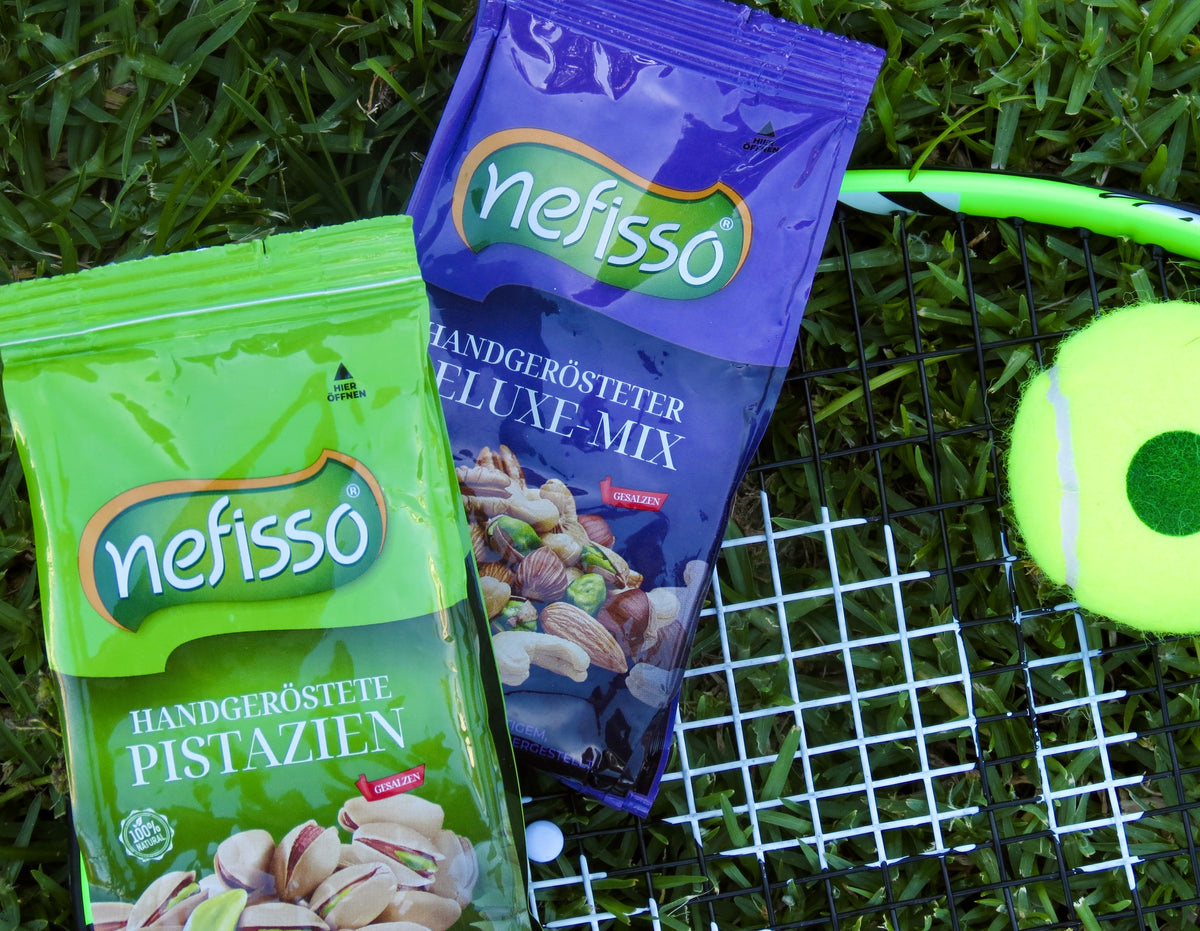Nefisso Pistazien und Deluxe Mix neben einem Tennisschläger auf dem Rasen